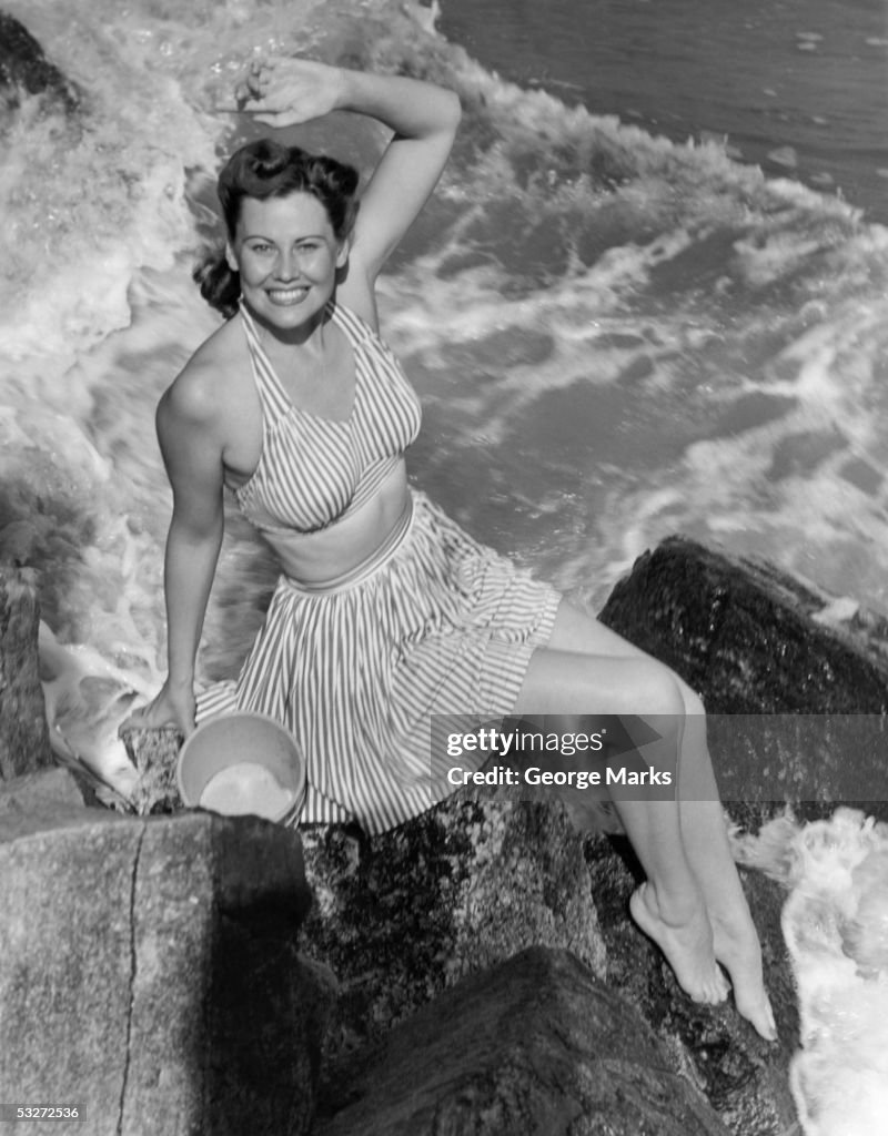 Woman in bathing suit sitting on rocks near waves