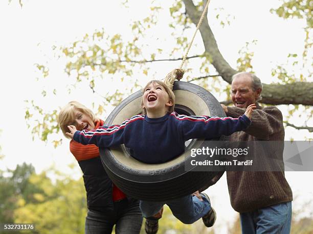 senior couple swinging boy on a tire swing - tire swing stock pictures, royalty-free photos & images