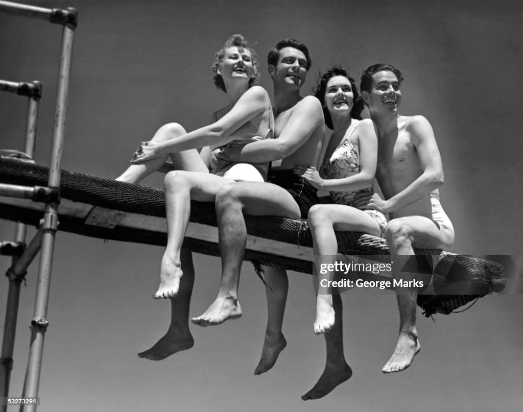 Two couples in bathing suits sitting on diving board