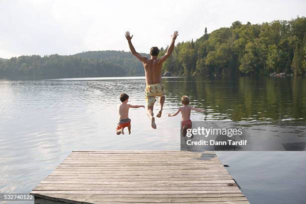 father and his sons jumping into lake - jumping into lake stock pictures, royalty-free photos & images