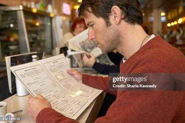 man looking at a menu in a diner - speisekarte stock-fotos und bilder