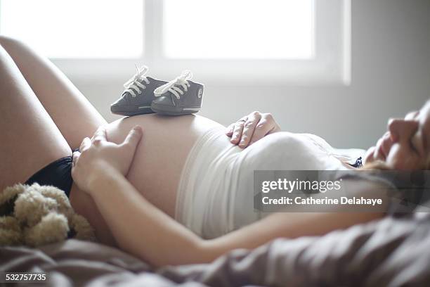 bootees on the womb of a 8 months pregnant woman - baby booties stock pictures, royalty-free photos & images