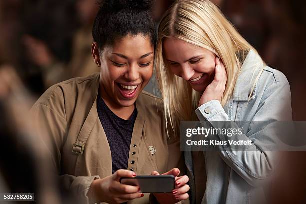 girlfriends looking at phone together among crowd - good news - fotografias e filmes do acervo