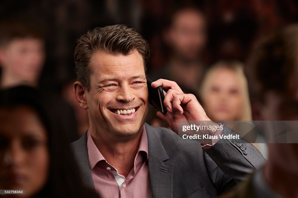 Businessman laughing, while on the phone, in crowd