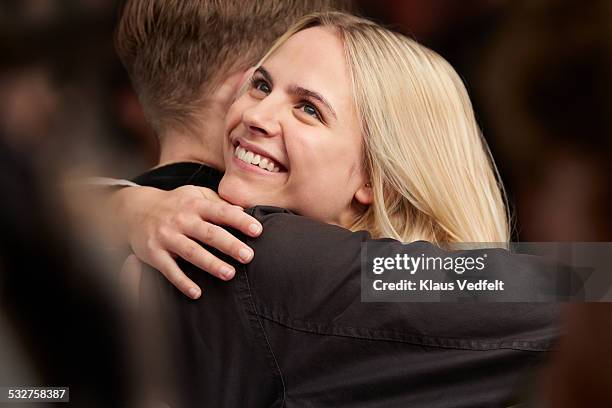 young couple hugging, standing in crowd - female blonde blue eyes stock-fotos und bilder