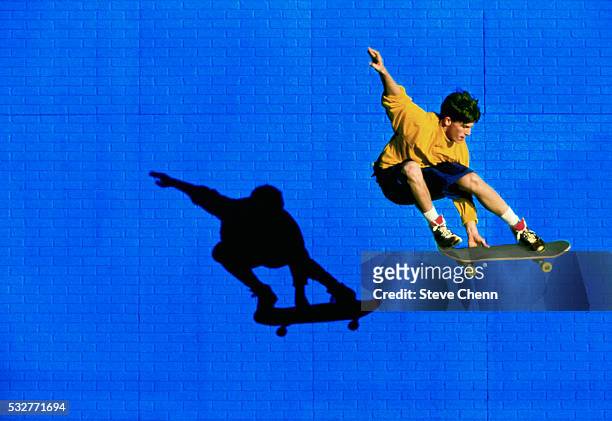 skateboarder flying past blue brick wall - skating stock pictures, royalty-free photos & images