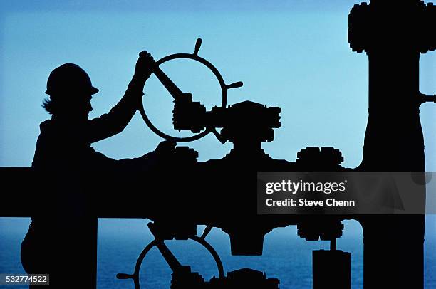 oil worker adjusting valve on pipe - oleodotto foto e immagini stock