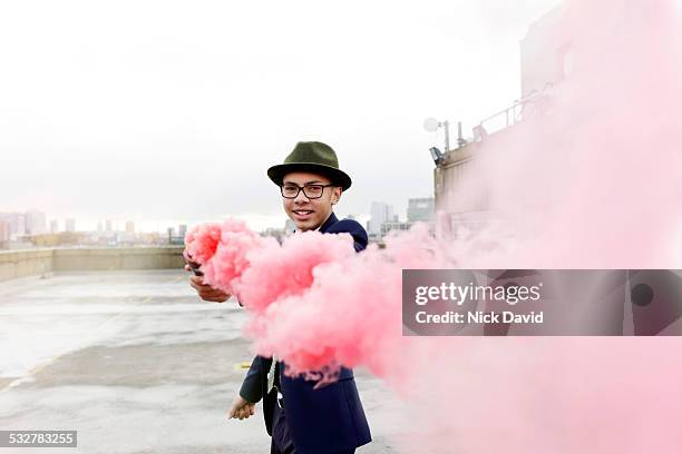 teenage boy on a rooftop over looking the city holding a pink smoking flare - distress flare stock pictures, royalty-free photos & images