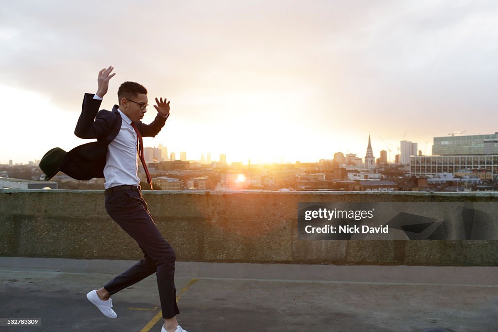 Teenage boy dressed in a cool suit jumping on a rooftop looking over the city
