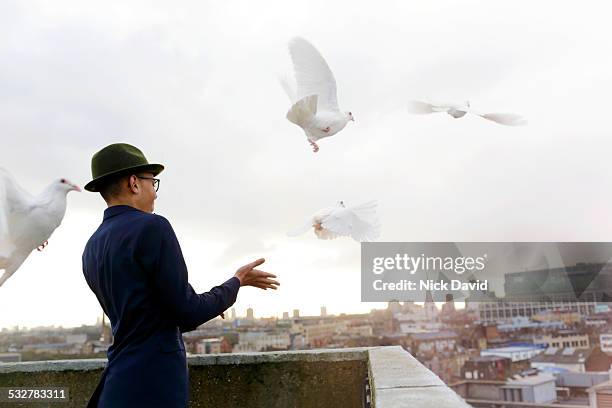 teenage boy releasing white birds from a rooftop in the city - releasing doves stock pictures, royalty-free photos & images