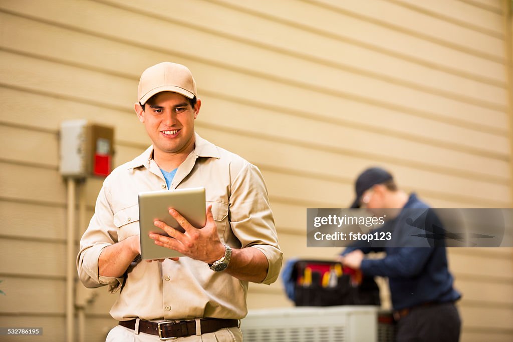 Air conditioner repairmen work on home unit. Blue collar workers.