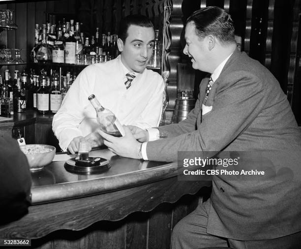 American restauranteur Bernard Toots Shor sits on a barstool and talks with bartender Frank Saunders, February 7, 1946.