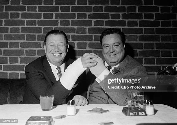 American restauranteur Bernard Toots Shor and American actor and entertainer Jackie Gleason smile as they clasp their cast-covered hands in Shor's...