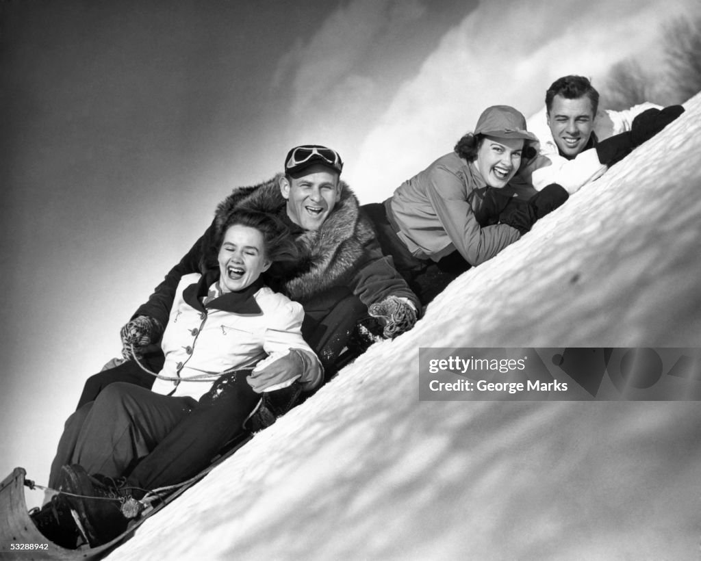 Two couples enjoying sled ride down hill