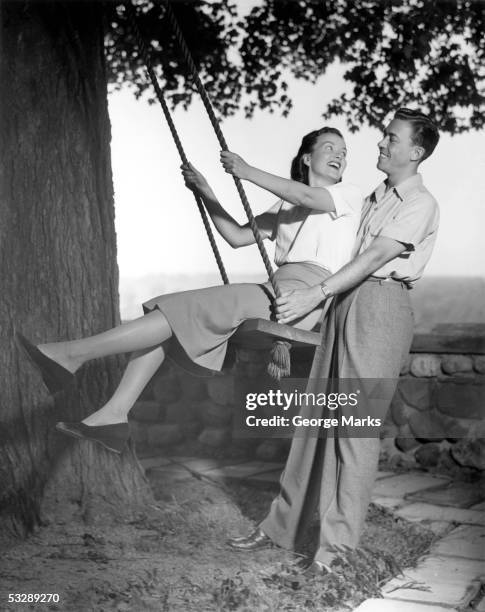 man pushing woman on swing hanging from - 1950s couple stock-fotos und bilder