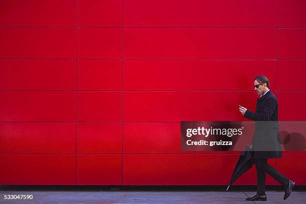 hübscher mann in schwarz gehen neben der roten wand - roter anzug stock-fotos und bilder