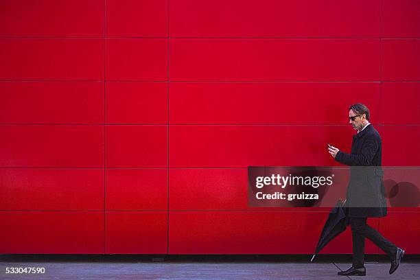 handsome man in black walking beside the red wall - red shirt stock pictures, royalty-free photos & images