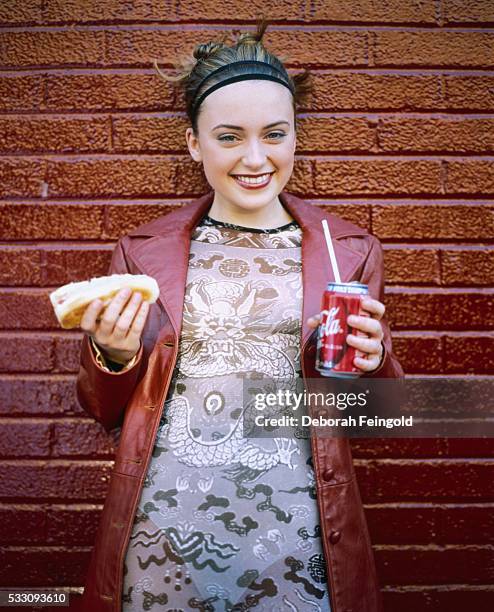 Deborah Feingold/Corbis via Getty Images) Actress Monica Keena stands next to a brick wall and holds a hot dog in one hand and a Coca-Cola can in the...