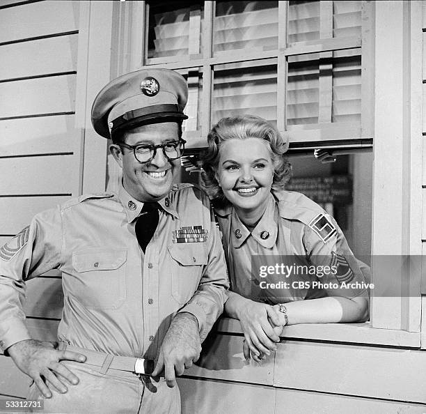 American actor Phil Silvers leans against a window sill as American actress Elisabeth Fraser looks out the window in an episode of the TV comedy...