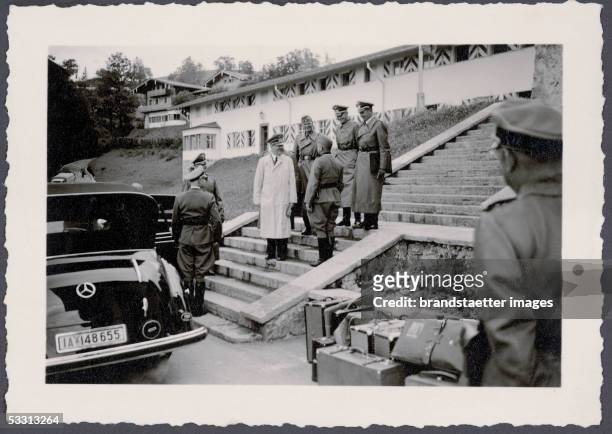 The Berghof of Adolf Hitler at the Obersalzberg near Berchtesgaden: Adolf Hitler wearing a white coat and a uniform bonnet, is standing on the stairs...