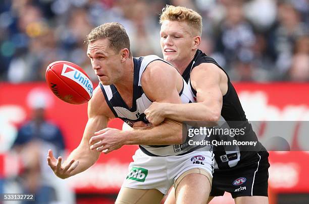 Joel Selwood of the Cats handballs whilst being tackled by Adam Treloar of the Magpies during the round nine AFL match between the Collingwood...
