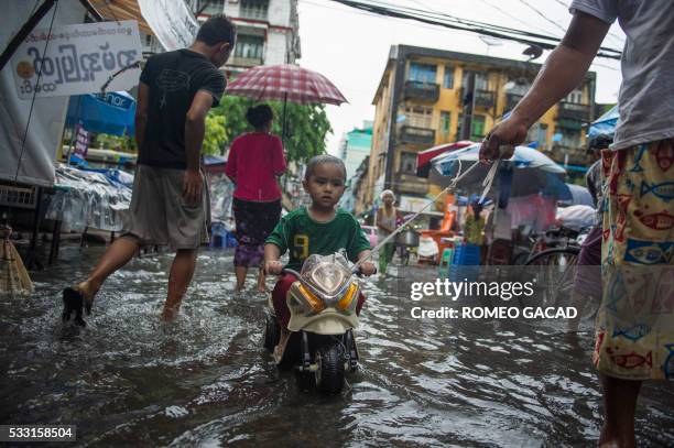 Boy rides a plastic toy motorcycle towed along a street partly submerged during heavy monsoon rains in Yangon on May 21 as long delayed rain brings...