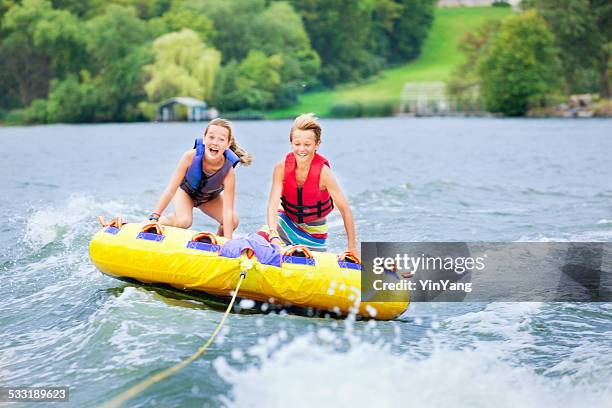 boy and girl children tubing on minnesota lake in summer - opblaasband stockfoto's en -beelden