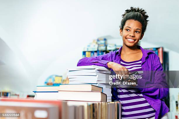 african-american high school girl on pile of books in library - alleen één tienermeisje stockfoto's en -beelden