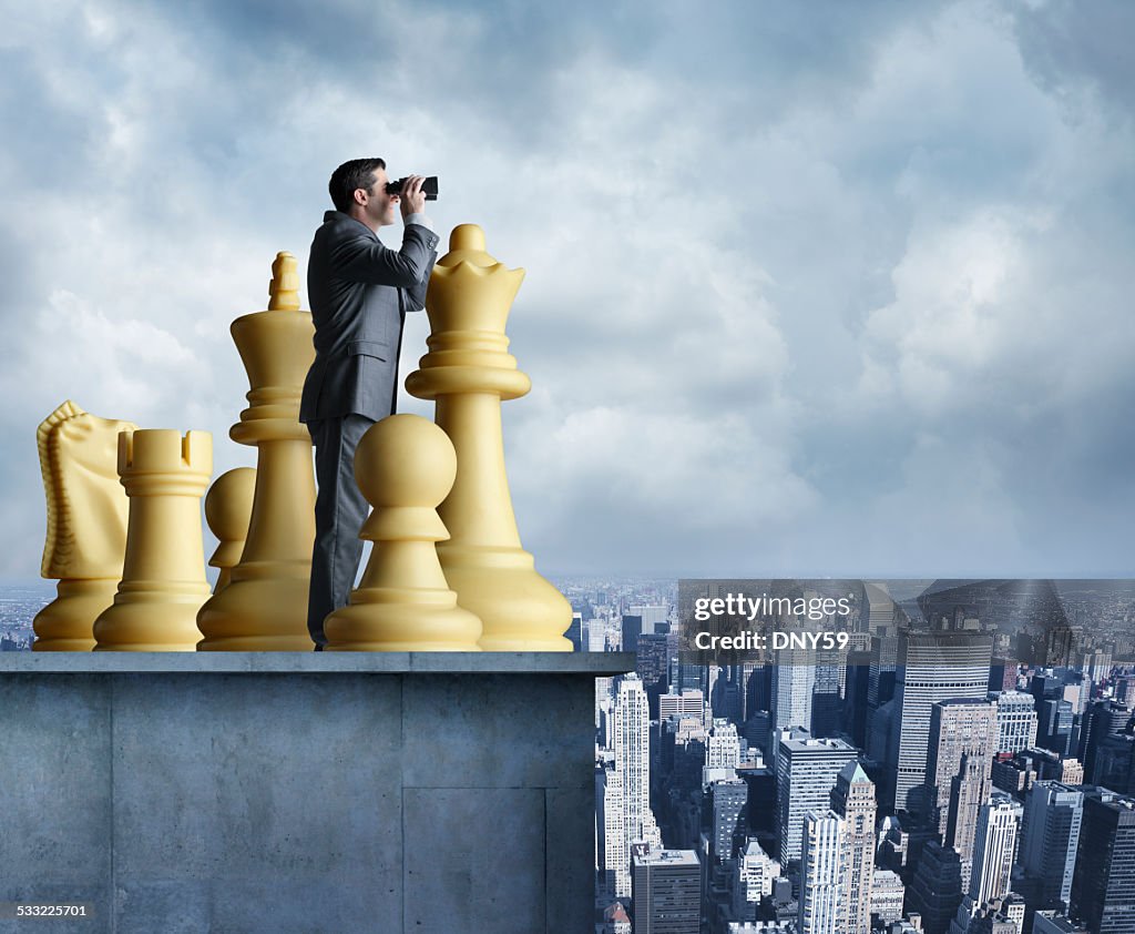 Businessman standing among chess pieces looks through binoculars