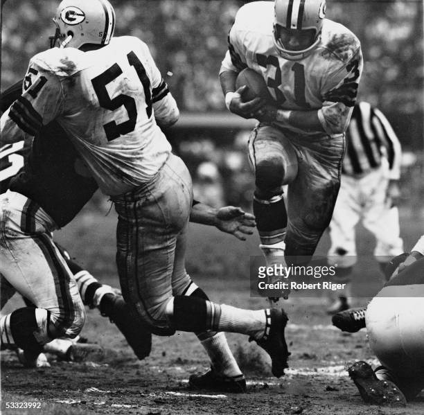 American professional football player Jim Taylor of the Green bay Packers runs with the ball through a gap in the defensive line of the Cleveland...