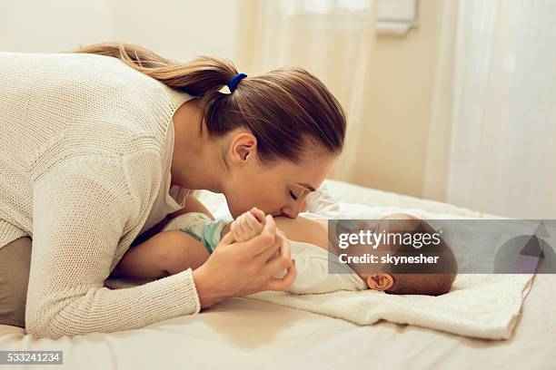 affectionate mother in bedroom kissing baby's belly. - baby abdomen stock pictures, royalty-free photos & images