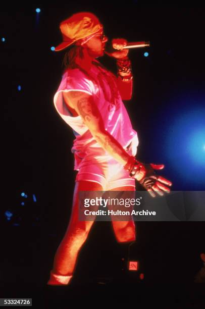 American rock singer Axl Rose of the band Guns N' Roses performs on stage, dressed in a white tank top and bike shorts, a backwards baseball cap, and...