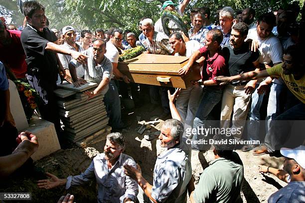Adel Turki, bottom left, gestures from an empty double grave as the coffins of his two daughters Hazar Turki and Dina Turki are lowered to their...