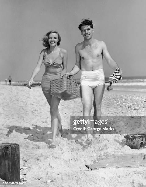 couple walking with picnic basket on beach - vintage swimwear stock pictures, royalty-free photos & images
