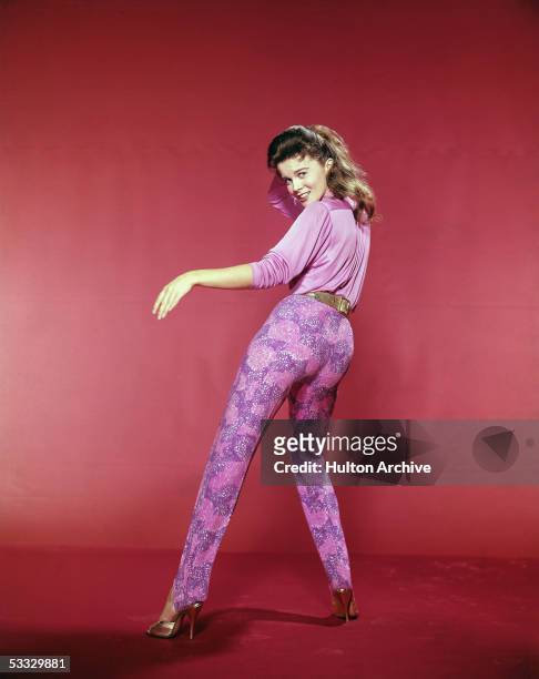 Studio portrait of Swedish-born actress and dancer Ann-Margret, wear a blouse, leggings and high heels, dancing while looking over her shoulder at...