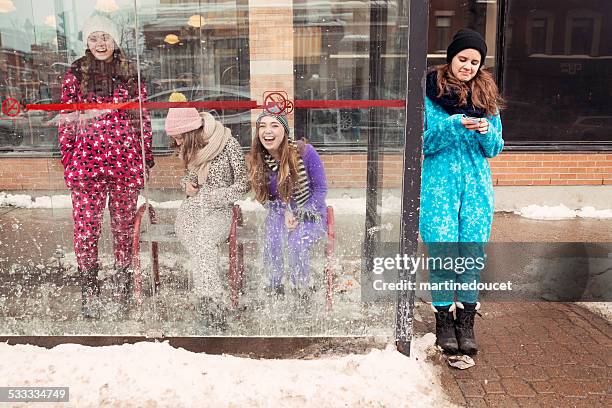 four young women wearing onesies waiting for bus in winter. - montreal street stock pictures, royalty-free photos & images