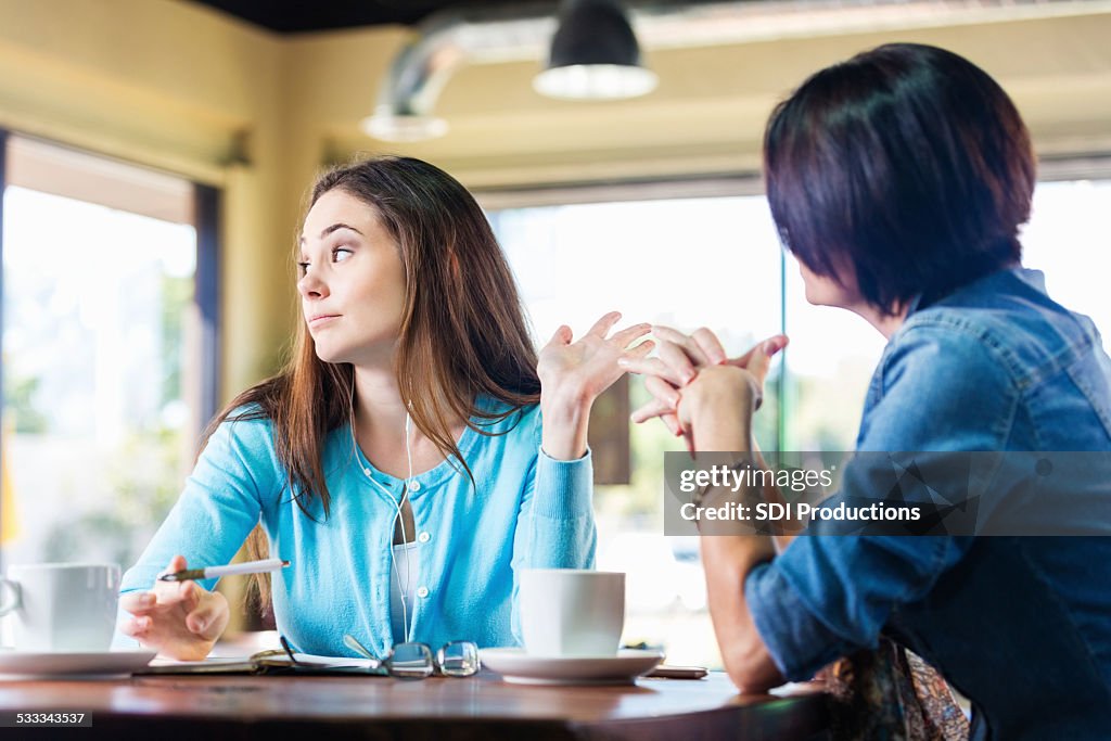 Annoyed teen girl talking to mother in coffee shop