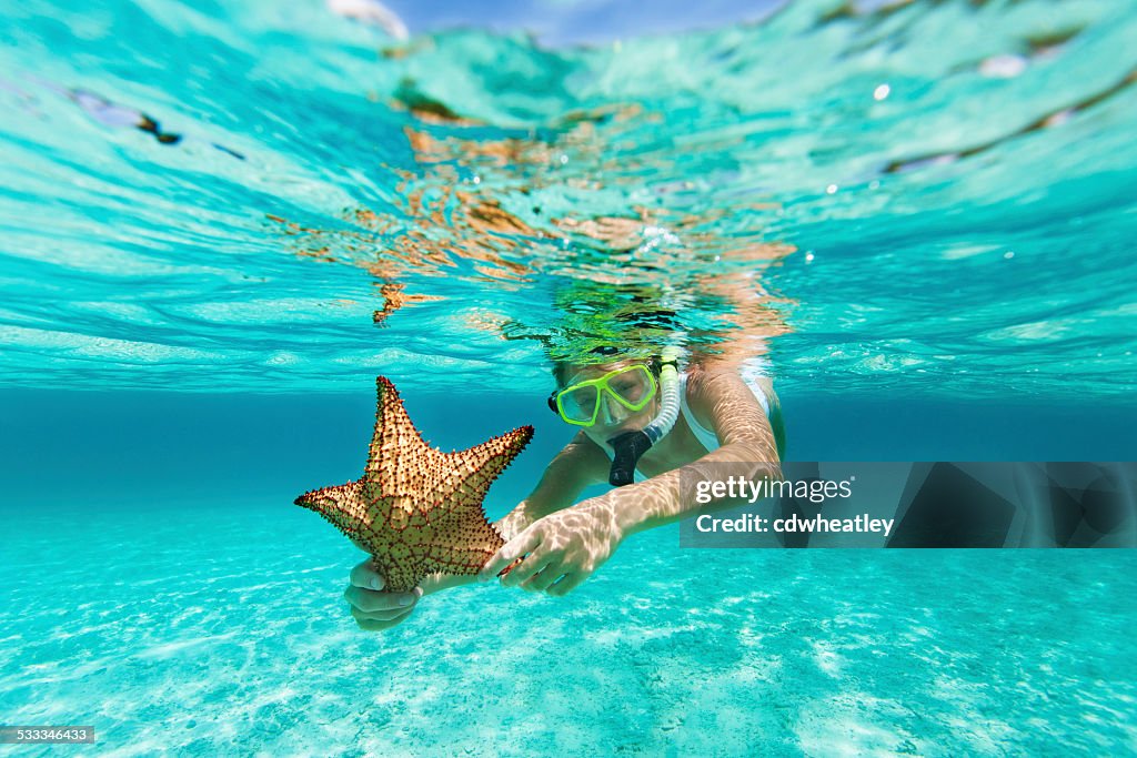 Mulher com máscara de mergulho e segurando uma estrela-do-mar