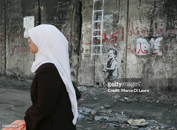 Palestinian woman passes by a graffiti entitled "Escapism" made by the British guerrilla, graffiti artist Banksy, is seen on August 6, 2005 on...