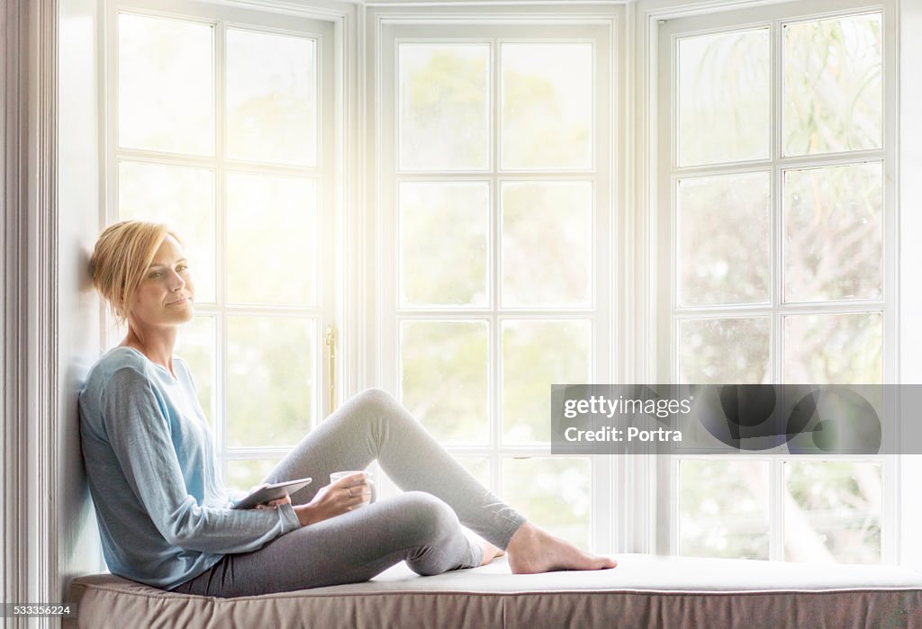 Thoughtful young woman relaxing on window sill