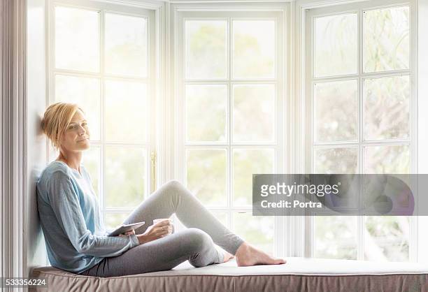thoughtful young woman relaxing on window sill - window sill 個照片及圖片檔
