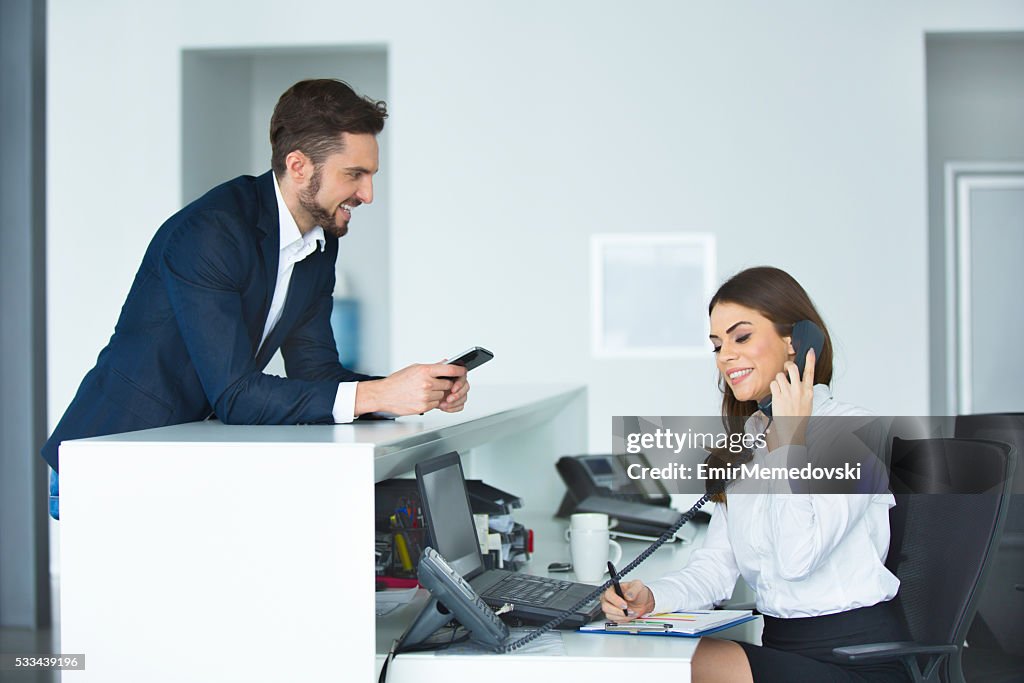 Smiling businessman and female receptionist at the secretary desk.