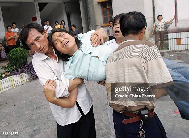 Relatives carry a family member of a miner trapped in a flood at Daxing Colliery, as she faints at a primary school on August 9, 2005 in Xingning of...