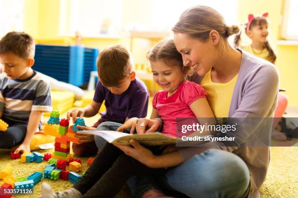 lächelnd kleines mädchen und lehrer lesen eine geschichte bereits im kindergarten an. - kindergarten stock-fotos und bilder