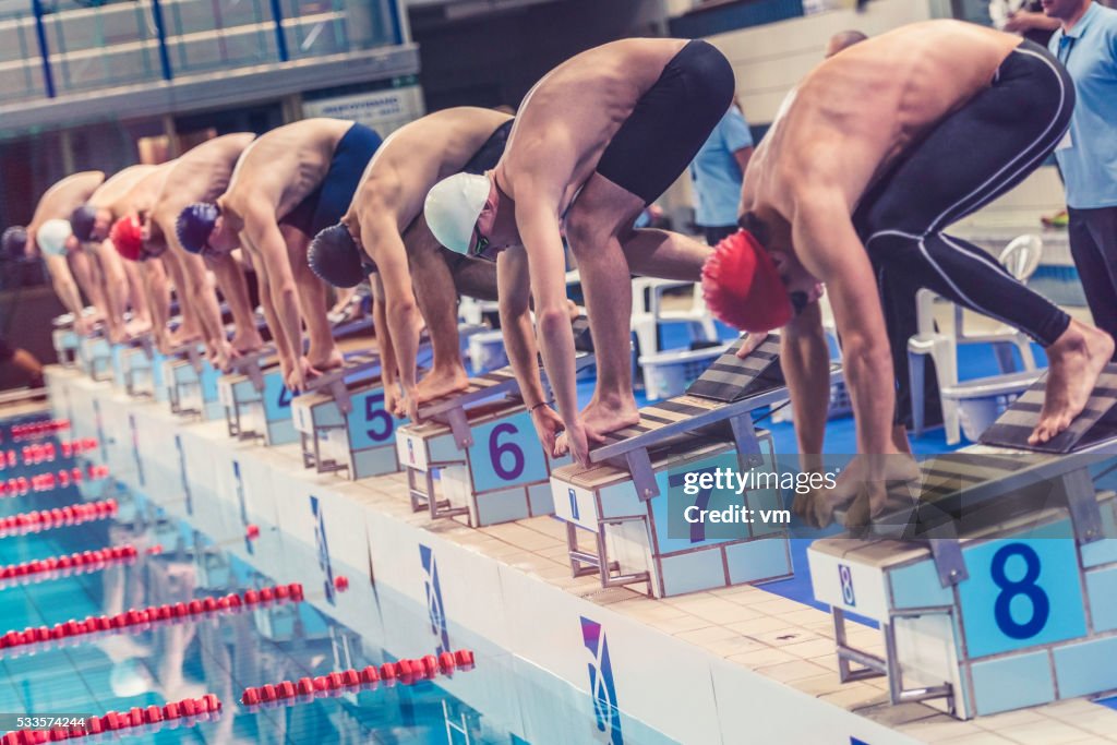 Swimmers crouching on starting block ready to jump