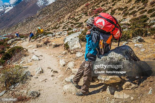 sherpa porter carrying expedition kit on himalaya mountain trail nepal - portier stockfoto's en -beelden