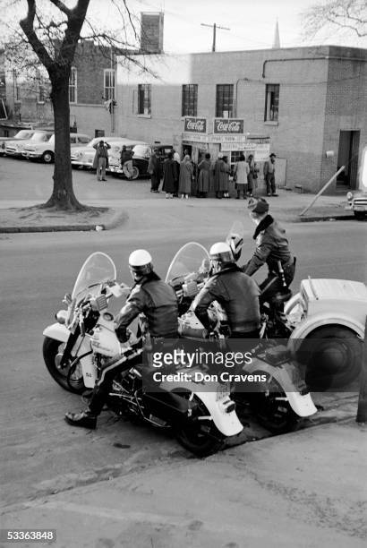 Three motorcycle police officers watch a small crowd of African Americans who wait for a car pool ride during the bus boycott, Montgomery, Alabama,...
