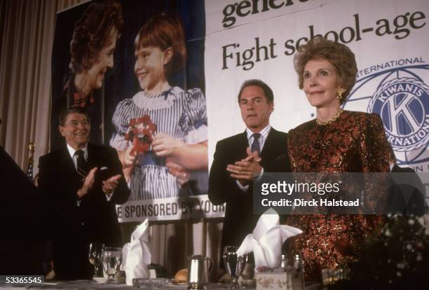First lady Nancy Reagan being applauded by President Ronald Reagan & unidentified at tribute for her work against drugs with poster of her in...