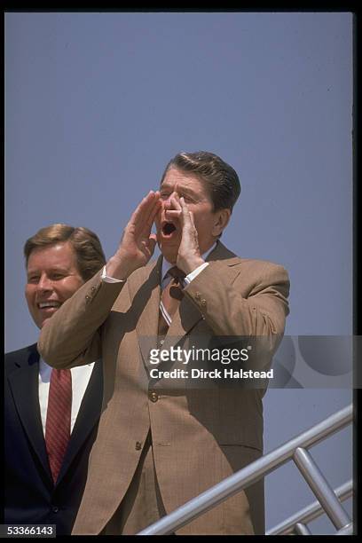 President Reagan poised before boarding Marine One, cupping mouth with hands, shouting response to press, with Representative Bob McEwen .