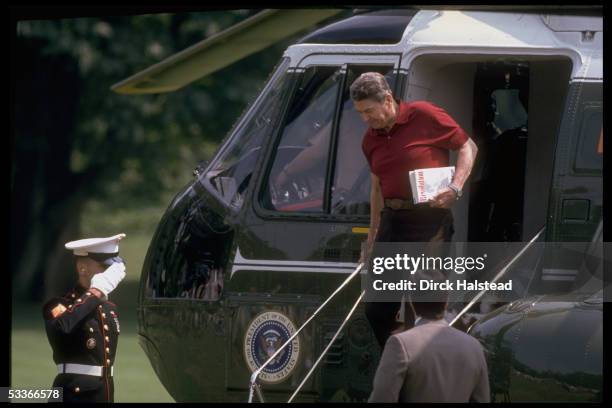 President Ronald Reagan deplaning Marine One carrying copy of book REVOLUTION by ex-financial adviser Martin Anderson, with saluting soldier.